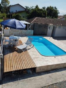 a pool with a deck and chairs and an umbrella at Casa de praia com piscina para 10 pessoas in São Francisco do Sul