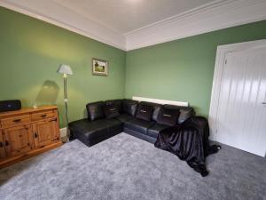 sala de estar con sofá de cuero negro y paredes verdes en 5 Bedroom modern home with parking. Near Brecon Beacons & Bike Park Wales, en Merthyr Tydfil