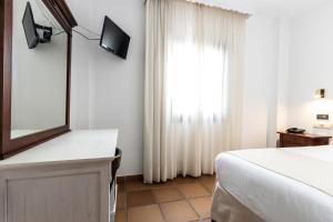 a bedroom with a bed and a mirror and a window at Hostal La Muralla in Zahara de los Atunes