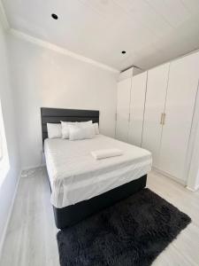 een witte slaapkamer met een groot bed en een zwart tapijt bij Fiore Apartments. in Kaapstad