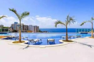 uma piscina com mesas e palmeiras e o oceano em Melhor vista de Salvador, apartamento 59.03m2. em Salvador
