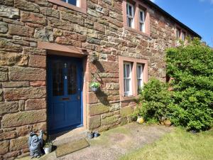 a stone house with a blue door and a cat sitting outside at 3 Bed in Appleby 86428 in Long Marton