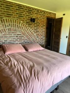 a bed with two pink pillows in front of a brick wall at Refugio Sereno in Puerto Octay