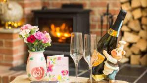 a table with two wine glasses and flowers and a fireplace at Piglet Cottage in Pebworth