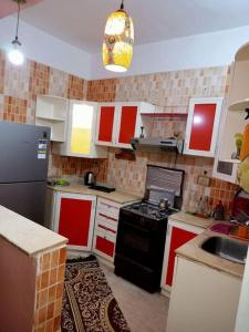- une cuisine avec des placards rouges et blancs et un réfrigérateur noir dans l'établissement El manzel, à Assouan