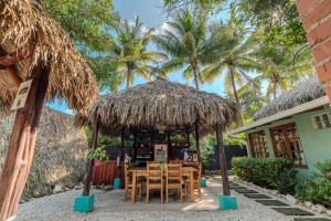 a table and chairs under a straw hut with palm trees at Playa Grande Surf Camp in Playa Grande