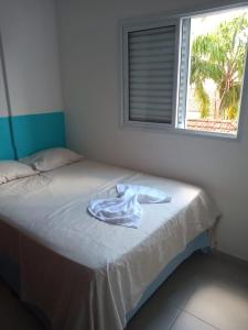 ein weißer Bademantel auf einem Bett mit Fenster in der Unterkunft Apartamento 2 quartos próximo da praia in Praia Grande