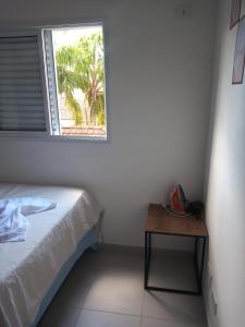 Schlafzimmer mit einem Bett, einem Fenster und einem Tisch in der Unterkunft Apartamento 2 quartos próximo da praia in Praia Grande