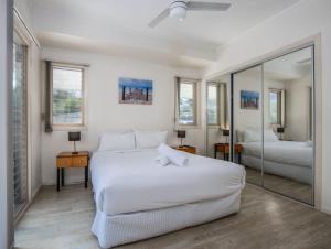een witte slaapkamer met 2 bedden en een spiegel bij Hastings Cove Holiday Apartments in Hastings Point