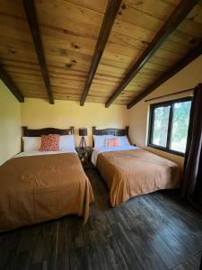 two beds in a room with wooden ceilings and wood floors at Cabaña No.7 Puerta del Bosque Mazamitla. in Mazamitla