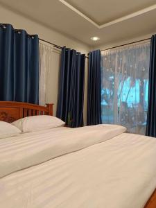 2 camas en un dormitorio con cortinas azules y ventana en บ้านระเบียงเลหลังสวน ทั้งหลัง 2 นอน 2 น้ำ 1 ครัว, en Ban Hin Sam Kon