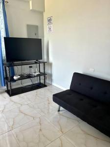 a living room with a black couch and a flat screen tv at Piarco Airport Guest House in Piarco