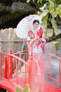 Eine Frau im Kimono, die einen Regenschirm auf einer Brücke hält. in der Unterkunft เรียวกัง ปาร์ค รีสอร์ท สไตล์ญี่ปุ่น Ryokan Park Resort in Ban Nam Dam