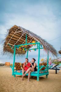 a man and woman sitting on a bench under an umbrella on the beach at Smile Beach Home in Galle