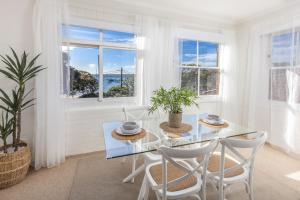 uma sala de jantar branca com uma mesa de vidro e cadeiras em Luxe-Coastal Balmoral Beachfront Apartment em Sydney