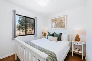 a white bedroom with a bed and a window at Canguri Boutique - A Memorable Farmstay near Mudgee in Mudgee