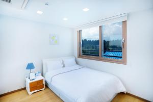een witte slaapkamer met een bed en een raam bij The Naeun Stay in Seogwipo
