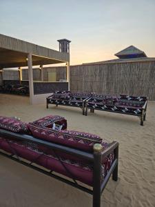 un grupo de bancos sentados en la arena cerca de un edificio en Desert Safari Overnight Experience "Modern room with AC & Entertainment", en Hunaywah
