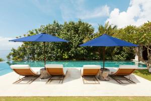 a group of chairs and umbrellas next to a swimming pool at The Ungasan Clifftop Resort in Uluwatu