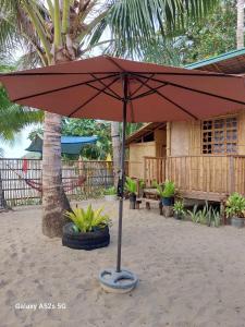 un parapluie rouge dans le sable devant une maison dans l'établissement Kubo Inn & Beach Camp, à El Nido