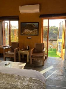 a bedroom with a bed and two chairs and a table at Prakriti Aalay - Riverside Mountain View Boutique Eco Resort in Dharamshala