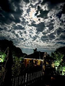 a cloudy sky with a house and a fence at Prakriti Aalay - Boutique Eco Resort Dharamshala in Dharamshala