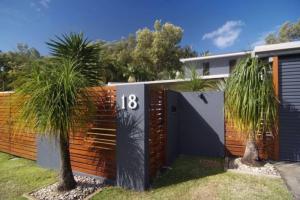 a fence with palm trees in front of a house at Bramston Beach - Premium Holiday House in Bramston Beach