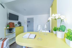 une table jaune avec deux verres à vin et des livres dans l'établissement Montempô Apparthôtel Evry, à Courcouronnes