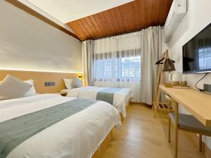 2 Betten in einem Zimmer mit einem Schreibtisch und einem TV in der Unterkunft Hemu House in Fenghuang