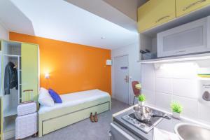 グッサンヴィルにあるMontempô apparthôtel CDG Goussainvilleのオレンジ色の壁の小さな客室で、ベッド1台が備わります。