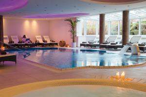 ein Pool in einer Hotellobby mit einer Frau, die daneben auf einem Stuhl sitzt in der Unterkunft l'Arrivée Hotel & Spa in Dortmund