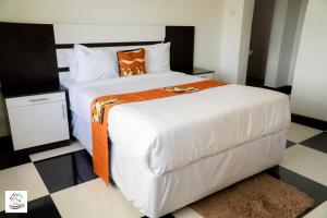a bedroom with a large white bed with an orange blanket at Likulezi Apartment 1 in Blantyre