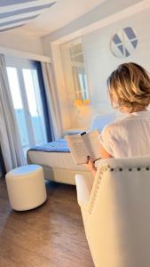 una mujer sentada en una silla leyendo un libro en un dormitorio en Hotel Panorama, en Cattolica