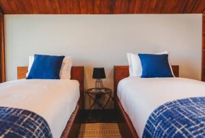 2 łóżka z białymi i niebieskimi poduszkami w pokoju w obiekcie Cabanas do Pico 1b w mieście São Roque do Pico