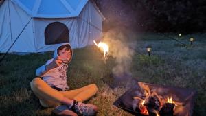 a young boy sitting next to a fire in front of a tent at Hideaway Escapes Rental Tents, 4 Unique tents NO BEDDING SUPPLIED in Narberth