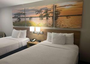 two beds in a hotel room with paintings on the wall at Days Inn by Wyndham Valdosta I-75 in Valdosta