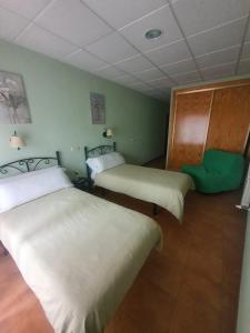 a room with two beds and a green chair at Hostal La Cigueña in El Espinar