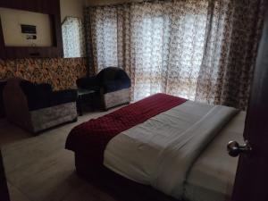 een slaapkamer met een bed, een stoel en gordijnen bij Hotel Rose Garden - Janakpuri in New Delhi