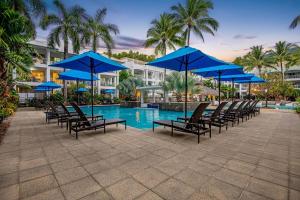 a group of chairs with blue umbrellas next to a pool at In the Tropics Balcony Oasis at The Beach Club in Palm Cove