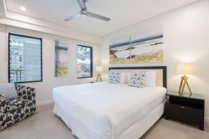 um quarto branco com uma cama e uma cadeira em Poolside Relaxation - Resort Retreat with Beach Access em Port Douglas