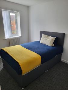 a bed with a blue and yellow blanket and a window at Larchmont House in Leicester