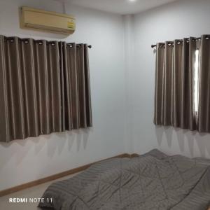 a bedroom with a bed and two windows with curtains at Bann Sukjai in Kanchanaburi City