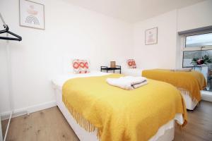 two beds in a white room with yellow blankets at Alma Cottage by StayStaycations in Rhondda