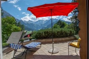 czerwony parasol i 2 krzesła na patio w obiekcie Chalet Grimm w mieście Adelboden