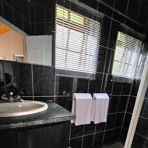 Baño de azulejos negros con lavabo y espejo en Grobler's Haven Self catering cottage, en Pretoria