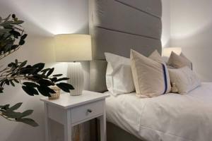 Forest Cwtch by Afan Valley Escapes في بورت تالبوت: سرير مع وسائد بيضاء وطاولة جانبية مع مصباح