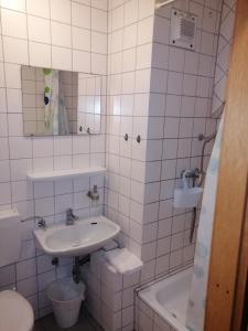 a white tiled bathroom with a sink and a tub at Zimmervermietung Gasthof Lamm, Zugang selbstständig über Schlüsseltresor in Dettingen unter Teck