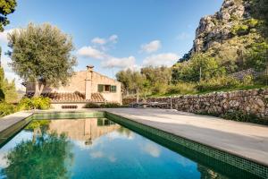 a swimming pool in front of a house with a stone wall at Finca Es Coste by Rentallorca in Pollença