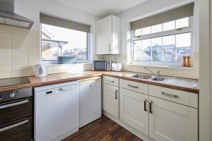 a kitchen with white cabinets and a sink and two windows at Host & Stay - Spring Gardens in Cayton