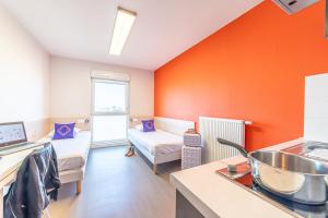 a kitchen with orange walls and a living room at Montempô Apparthôtel Toulouse Balma in Toulouse